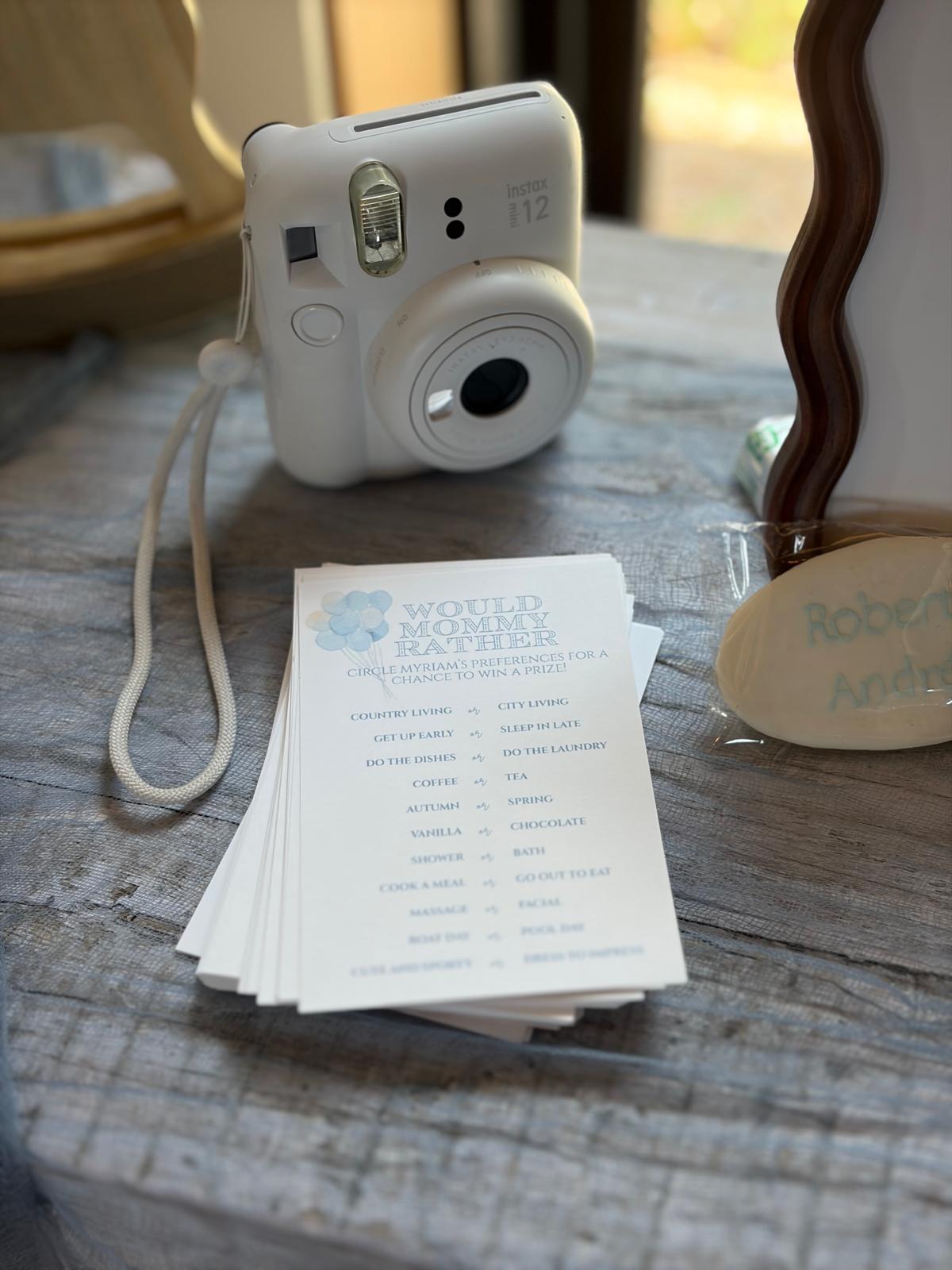 Stack of "Would Mommy Rather" baby shower game cards beside an instant camera